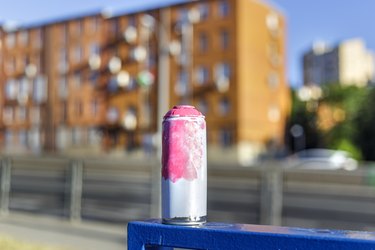 Outdoor spray paint can on blue metal bar with road and brick house block background