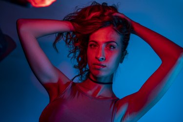 High Fashion model woman in colorful bright neon blue and purple lights posing in studio. Portrait of beautiful woman with trendy glowing make-up. Art design vivid style