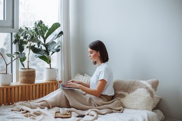 Young woman working on laptop at home in bed