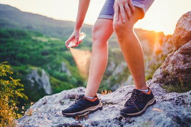 Woman using anti mosquito spray outdoors at hiking trip