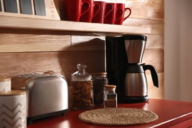 Modern coffeemaker and toaster on red table near wooden wall