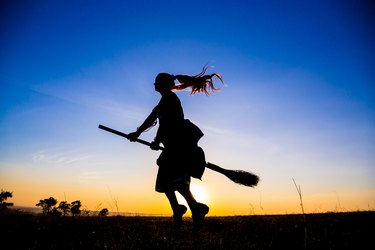 Silhouette of young witch flying on the broomstick at sky