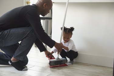 Black father and daughter using broom and dustpan