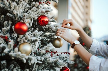 Cropped hand of woman decorating and hanging baubles on Christmas tree