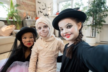 Happy halloween girl making selfie with two kids in costumes