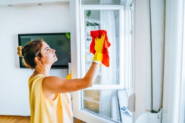 Beautiful smiling young woman cleaning and wiping window with spray bottle and rag stock photo