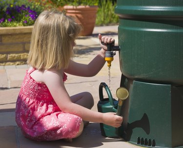 Young girl collecting water in a watering can from a water butt MR PR