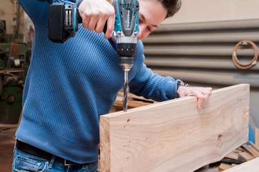 A man drills a board with an electric drill in a carpentry workshop. Close-up