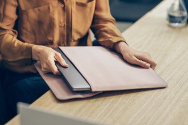 Hands of a Businesswoman Taking Out her Laptop Computer out of the Sleeve on her Desk