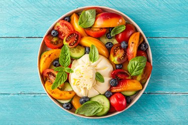 Delicious summer salad with burrata cheese, grilled peaches, tomatoes, blueberries, cucumber, olive oil and basil