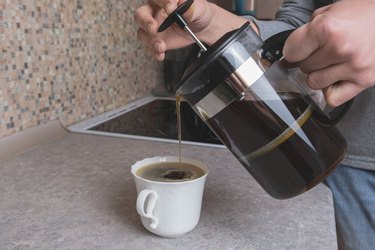 Woman pours coffee from a French press into a white porcelain cup