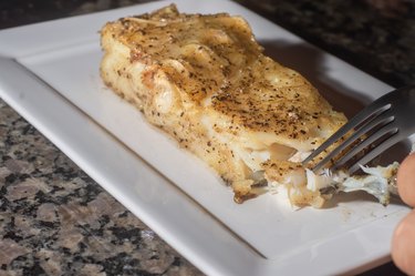 Fish sliced and roasted cod, on a white dish with copy space and dark background