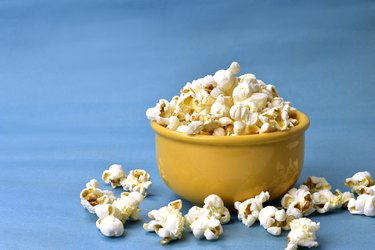 popcorn inside bowl with pink bottom with corn beside on blue background