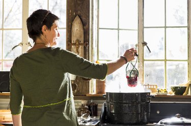 Rear view of woman removing beetroot preserves jar from steaming saucepan