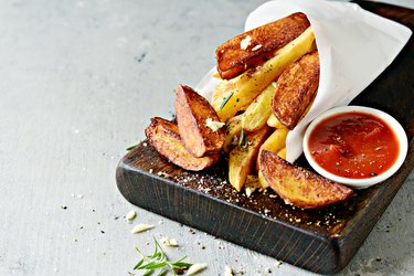 Baked rasted potato with spices and salt. Tasty french fries on cutting board with ketchup. Fast food concept