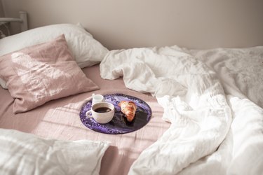 Handmade crystal violet epoxy resin decor tray with coffee cup and croissant on pink and white bed. Morning mood.
