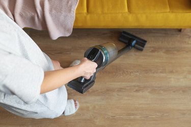 Woman holding wireless vacuum cleaner on a floor under yellow sofa