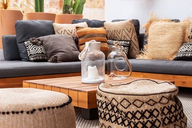 2 glass vases on a low wooden coffee table surrounded by two soft ottomans and a corner sofa with a heap of various cushions. Patio of Mediterranean villa