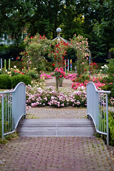 A garden with many flowers next to the path leading to the gazebo via a bridge