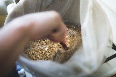 Close up of male hand stirring two row grain in pan for home brew beer