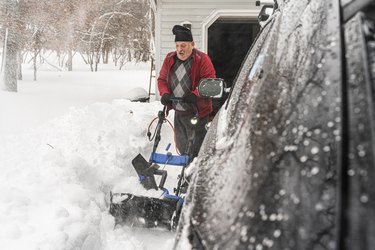 Senior man cleaning the snow in front of his garage using a snowblower.