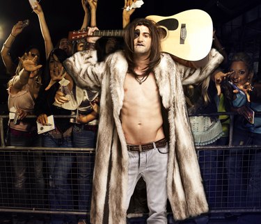 Portrait of young rock musician with guitar posing for excited audience at concert