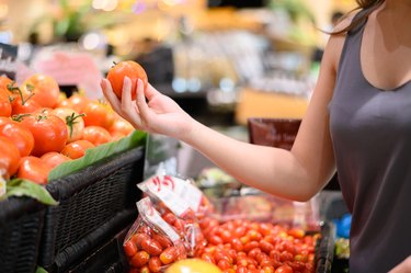 Young Asian woman picking up tomato at grocery store or supermarket