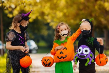 Three kid with a basket for sweets making grimaces wearing face mask on Halloween holiday