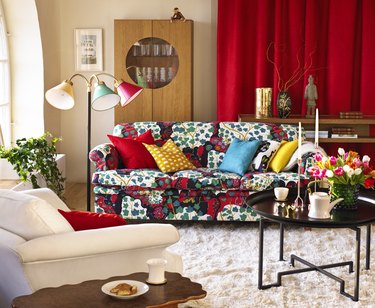 An eclectic living room with patterned couch, red curtains and a vase of tulips