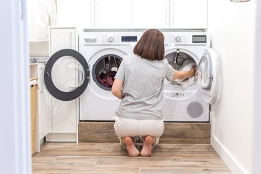 Woman Loading Dirty Clothes In Washing Machine For Washing In modern Utility Room