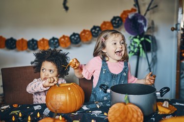 Two children at a table with a pumpkin taking out the middle and laughing.