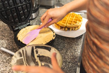 close-up of a woman's hands placing dough in a waffle iron