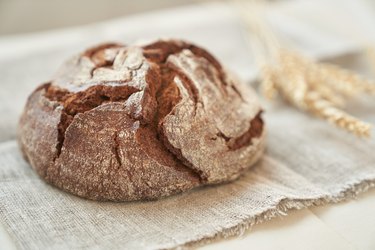 Freshly baked rye bread on a yeast-free starter and on a mixture of whole grain, rye and wheat flour. It lies on a napkin, next to a dried flower with grains. Selective focus
