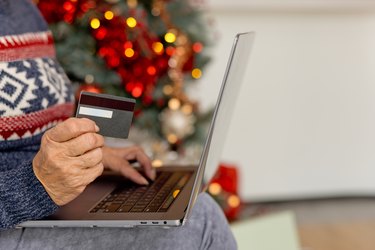 Close up of senior woman shopping online with portable laptop sitting on couch during festive Christmas season