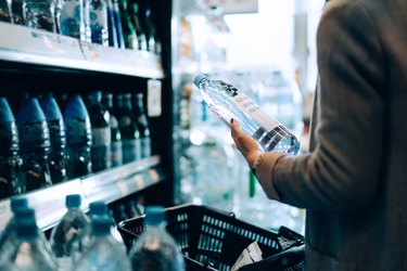 Close up of woman with shopping cart shopping for bottled water along the beverage aisle in a supermarket. Healthy eating lifestyle