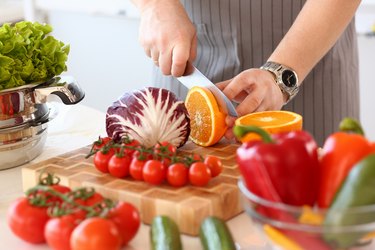 Man in apron cutting orange in kitchen