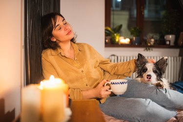 Young woman relaxing at home with her dog in bed with candles and hot drink,Poland