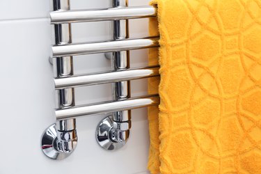 A yellow towel is dried on a heated towel rail.Heated Towel Rack. Polished Stainless Steel.Hotel Fabric. Wall style. Towel warmer for the bathroom.