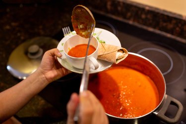 Woman pouring tomatoe soup from pot to bowl