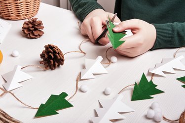 DIY Christmas home decor from natural materials. Hands make garland of paper trees, twine and cones