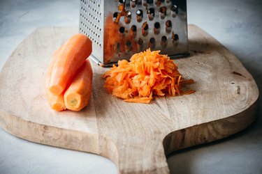 Whole and shredded carrot with box grater on a wood cuttng board
