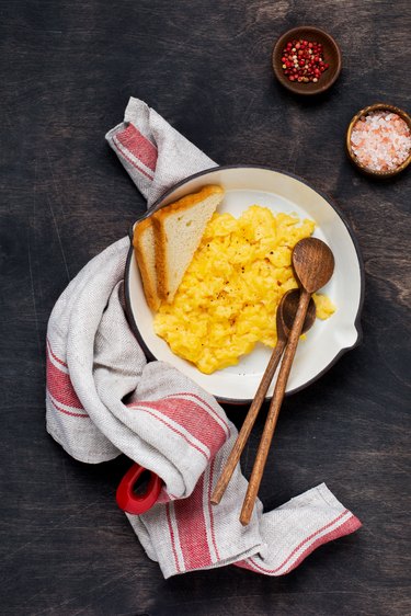 Scrambled eggs for breakfast on red old frying pan, dark wooden table background. Traditional English breakfast. Top view with cope space