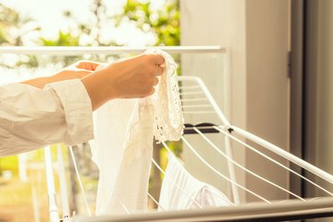 Woman check stains after washing. Female hanging her laundry on balcony on the drying rack opposite palm trees and sea view at sunset sunshine.