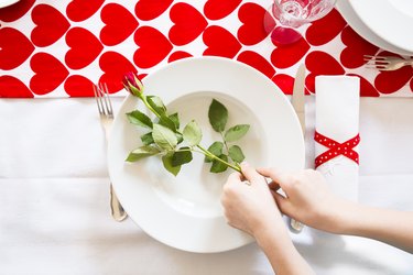 Hands putting rose on dish at laid table