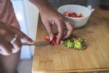Closeup of young woman chopping strawberries on cutting board