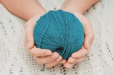blue ball of wool in hands on the background of a white knitted tablecloth