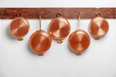 Row of shiny clean copper pans, different size, hung on wooden plank