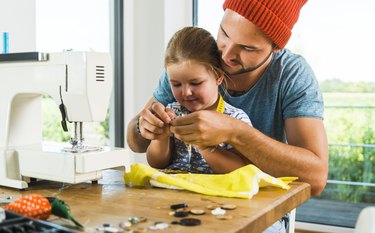 Father and daughter at home using sewing machine