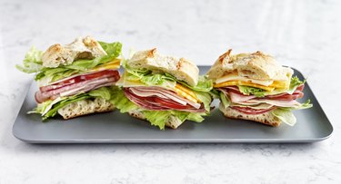 Sandwiches with salami, ham, cheese, and tomatoes on a tray on white background