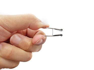 Close-Up Of Hand Holding Binder Clip Against White Background